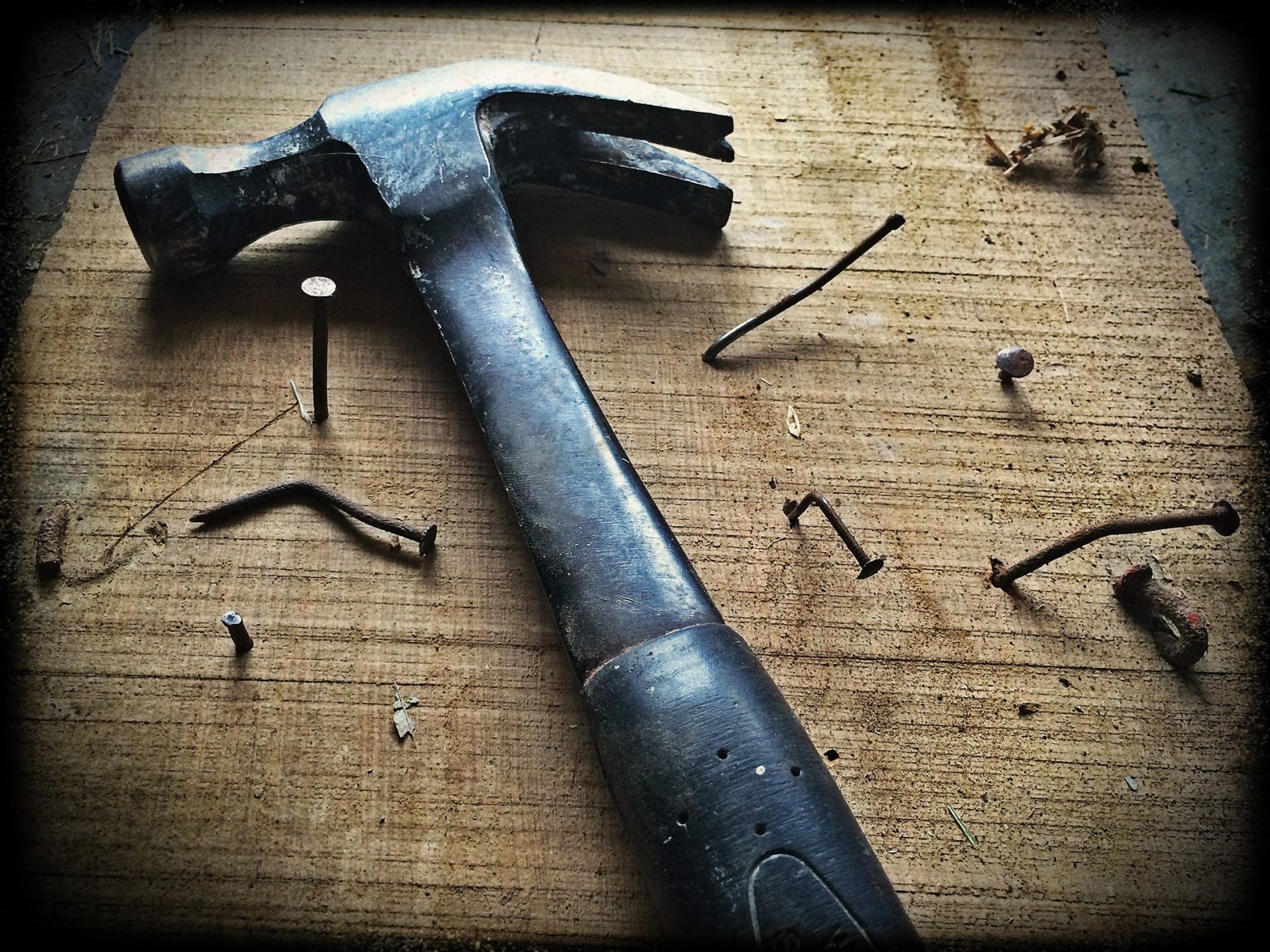 Hammer and many bent nails in a board.